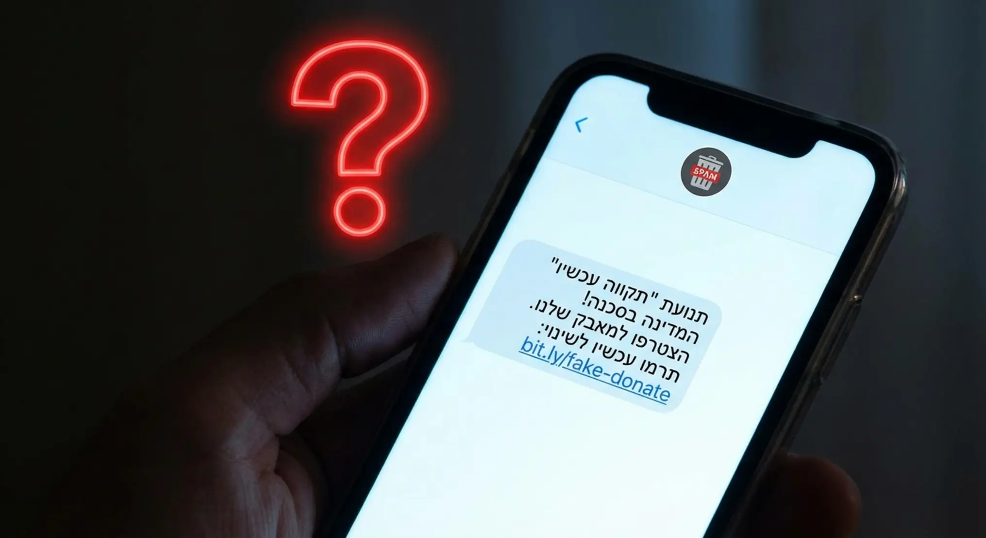 תקריב של מסך סמארטפון המציג הודעת SMS. ההודעה נשלחה לכאורה על ידי עמותה או גוף פוליטי, וטקסט ההודעה כולל קריאה לפעולה (למשל, 'תרום עכשיו' או 'הצבע למען X'). מעל המסך מרחף סימן שאלה גדול ומודגש, ובפינה יש אייקון של תיקיית 'ספאם' או 'ג'אנק'.