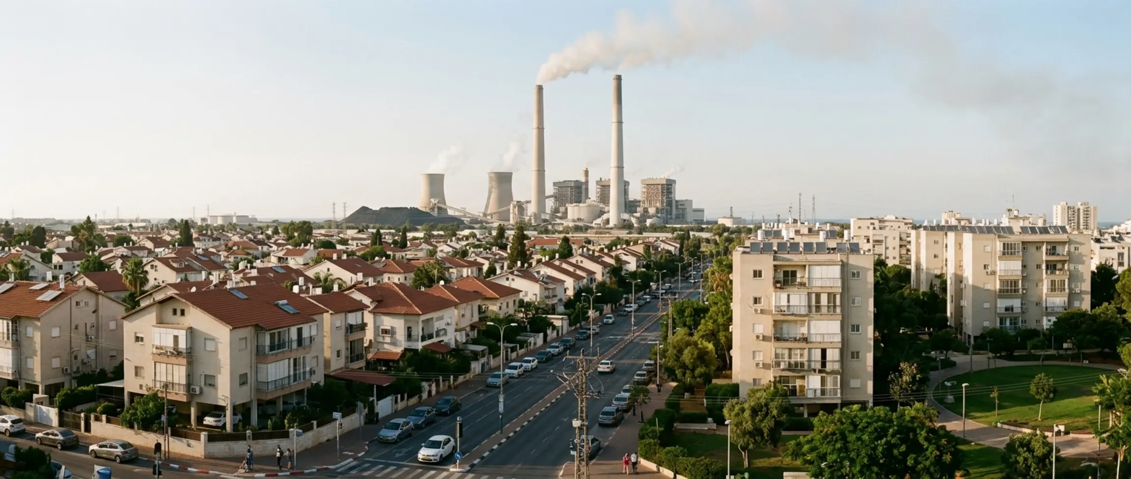 צילום פנורמי של שכונת מגורים בחדרה, כשברקע מתנשאות הארובות האיקוניות של תחנת הכוח "אורות רבין". התמונה מציגה שילוב בין בתי מגורי ותשתיות אזרחיות לבין המתחם התעשייתי המסיבי, הממחיש את הקרבה הגיאוגרפית שעמדה במוקד התביעה הייצוגית בגין מפגעי האבק והאפר.